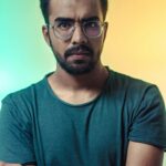 A thoughtful adult man with eyeglasses posing for a portrait with a vibrant backdrop.